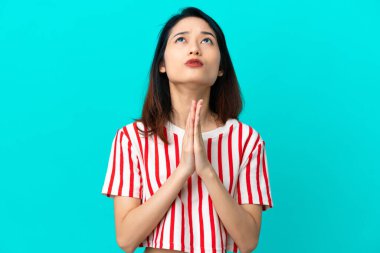 Mavi arka planda izole edilmiş genç Vietnamlı kadın avuç içlerini bir arada tutuyor. İnsan bir şey ister.