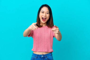 Genç Vietnamlı kadın mavi arka planda izole edilmiş şaşırmış ve ön tarafı işaret ediyor.