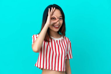 Mavi arka planda izole edilmiş genç Vietnamlı kadın parmaklarıyla tamam işareti gösteriyor.