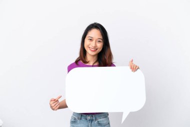 Beyaz arka planda izole edilmiş genç Vietnamlı bir kadın boş bir konuşma balonu tutuyor ve onu işaret ediyor.
