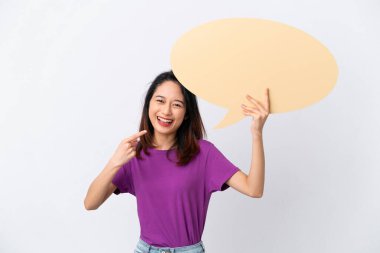 Beyaz arka planda izole edilmiş genç Vietnamlı bir kadın boş bir konuşma balonu tutuyor ve onu işaret ediyor.
