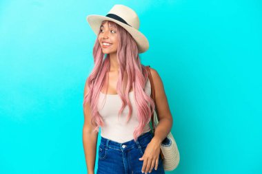 Mavi arka planda Pamela izole edilmiş plaj çantası tutan genç bir ırk kadını.