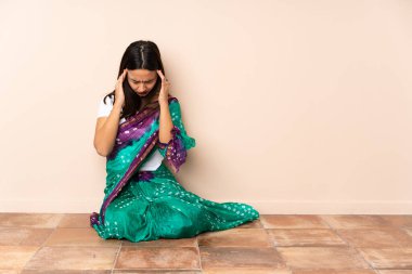 Genç Hintli kadın baş ağrısıyla yerde oturuyor.