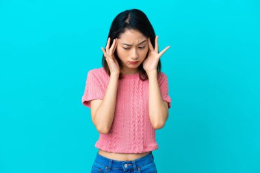 Genç Vietnamlı kadın mavi arka planda izole edilmiş, baş ağrısı var.
