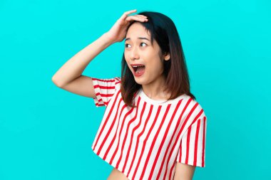 Mavi arka planda izole edilmiş genç Vietnamlı kadın yan tarafa bakarken sürpriz jest yapıyor.