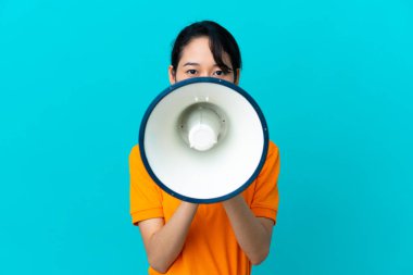 Genç Vietnamlı kadın mavi arka planda izole edilmiş megafonla bir şey duyurmak için bağırıyor.