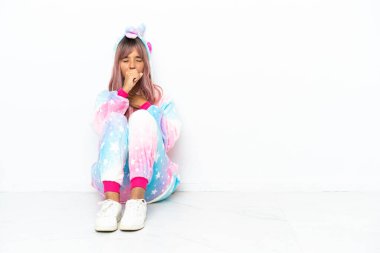 Beyaz arka planda tek boynuzlu at pijaması giyen genç melez kadın öksürüp kendini kötü hissediyor.