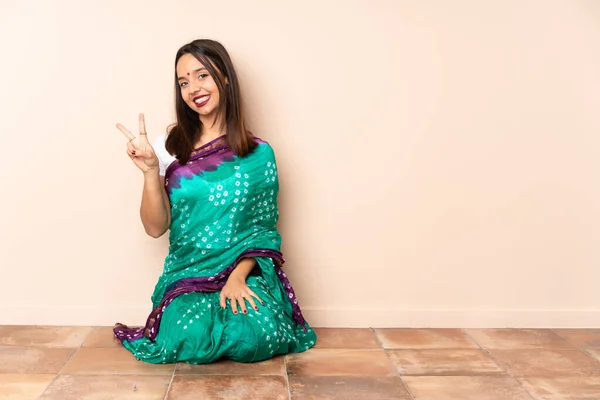 Młoda Hinduska Kobieta Siedząca Podłodze Uśmiechnięta Pokazująca Znak Zwycięstwa — Zdjęcie stockowe