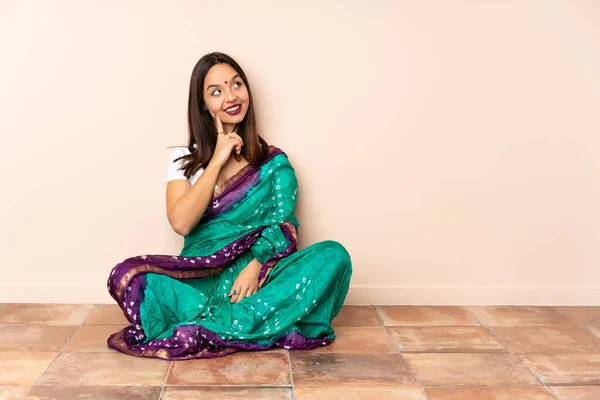 Young Indian woman sitting on the floor thinking an idea while looking up
