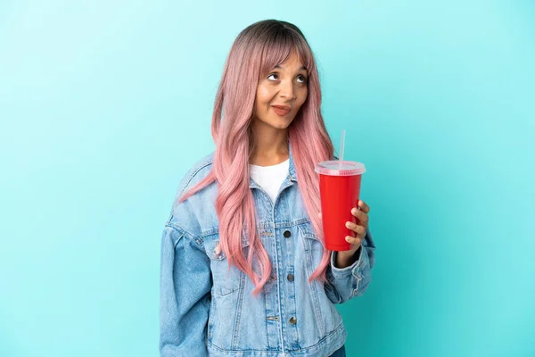 若い混合人種の女性が青の背景に隔離された新鮮な飲み物を飲んで検索 — ストック写真