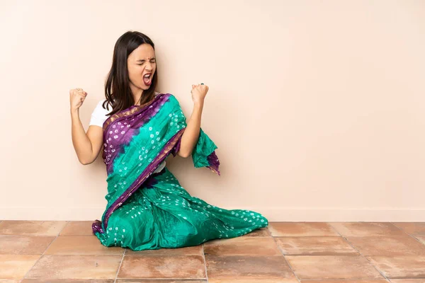 Young Indian woman sitting on the floor doing strong gesture