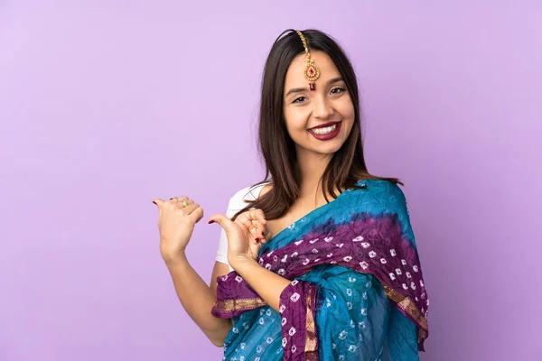 製品を提示するために側面を指す紫色の背景に隔離された若いインド人女性 — ストック写真