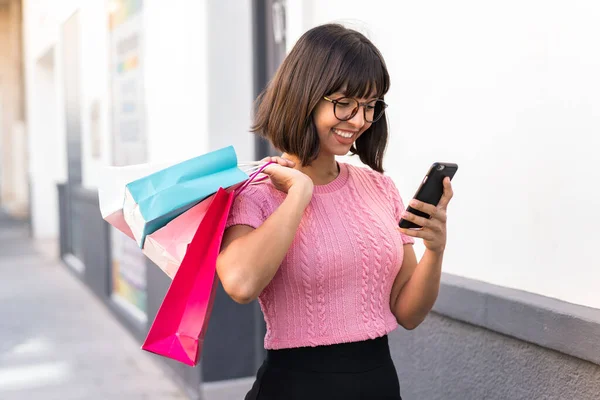 Mladá Brunetka Žena Městě Drží Nákupní Tašky Psaní Zprávy Mobilním — Stock fotografie