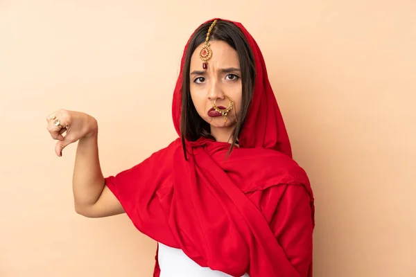 若いですインドの女性は 負の式で親指を下に示すベージュの背景に隔離 — ストック写真