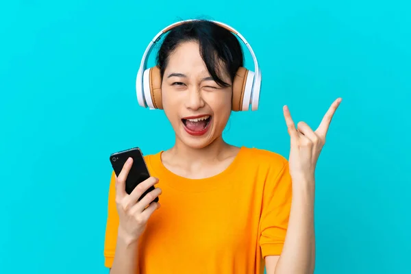 Young Vietnamese Woman Isolated Blue Background Listening Music Mobile Making — Fotografia de Stock