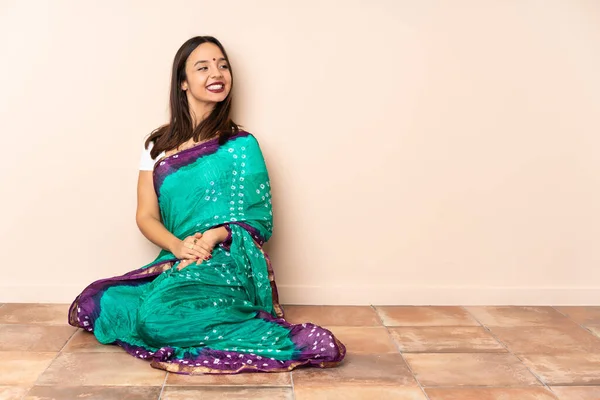 Young Indian woman sitting on the floor looking to the side and smiling