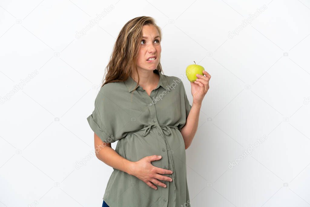 Young caucasian woman isolated on white background pregnant and frustrated while holding an apple