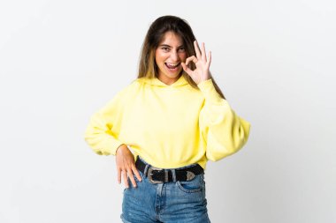 Beyaz arka planda izole edilmiş genç beyaz kadın parmaklarıyla tamam işareti gösteriyor.