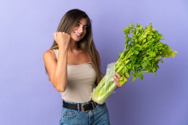 Mor arka planda izole edilmiş kereviz taşıyan genç bir kadın zaferi kutluyor.