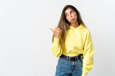 Beyaz arka planda izole edilmiş genç beyaz kadın mutsuzdu ve kenarı gösteriyordu.