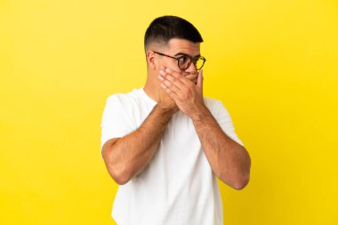 Genç yakışıklı adam, izole edilmiş sarı arka planda ağzını kapatıyor ve yan tarafa bakıyor.