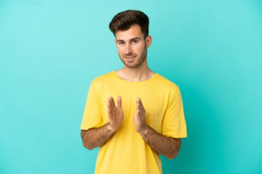 Beyaz tenli yakışıklı adam mavi arka planda izole edilmiş bir konferansta sunumdan sonra alkışlıyor.