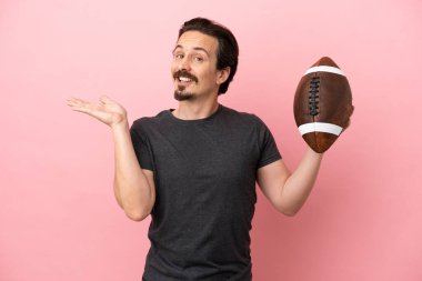 Genç beyaz adam rugby oynuyor. Pembe arka planda izole edilmiş. Gelmesi için ellerini yana uzatıyor.