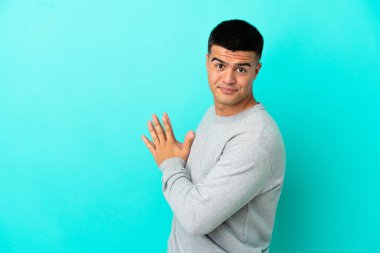 Soyutlanmış mavi arka planda genç yakışıklı bir adam bir şeyler planlıyor.