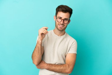 Genç beyaz yakışıklı adam mavi arka planda izole edilmiş gülüyor.