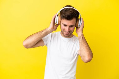 Sarı arka planda izole edilmiş beyaz yakışıklı bir adam müzik dinliyor.