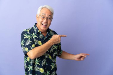 Mor arka planda izole edilmiş orta yaşlı Brezilyalı adam şaşırmış ve işaret ediyor.