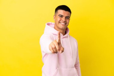 Soyutlanmış sarı arka planda genç yakışıklı adam parmağını kaldırıyor ve gösteriyor.
