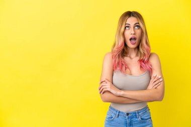 Soyutlanmış sarı arka planda genç bir kadın yukarı bakıyor ve şaşırmış bir ifadeyle