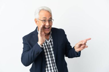 Orta yaşlı Brezilyalı bir adam beyaz arka planda izole edilmiş bir şekilde bir ürün sunmak ve bir şeyler fısıldamak için kenarı işaret ediyor.