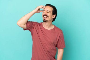 Kafkasyalı genç adam mavi arka planda izole edilmiş, çok gülümsüyor.