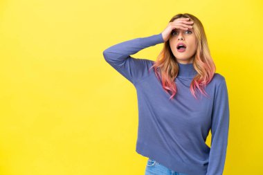Yalıtılmış sarı arka planı olan genç bir kadın yan tarafa bakarken sürpriz jest yapıyor.