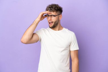 Teslimat yapan beyaz adam mor arka planda izole edilmiş. Yan tarafa bakarken sürpriz jest yapıyor.