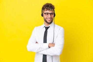 Sarı arka planda kolları bağlı ve mutlu bir kulaklıkla çalışan pazarlamacı sarışın bir adam.