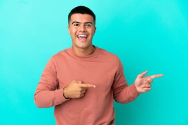 Soyutlanmış mavi arka planda genç yakışıklı adam şaşırmış ve işaret ediyor.