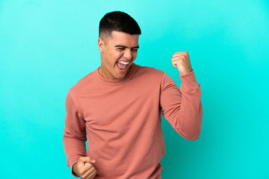 Soyutlanmış mavi arka planda genç yakışıklı bir adam zaferi kutluyor.