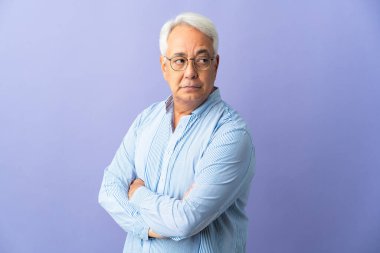 Mor arka planda izole edilmiş orta yaşlı Brezilyalı adam kollarını kavuşturuyor.