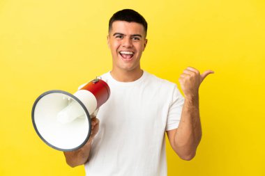 Soyutlanmış sarı arka planda genç yakışıklı adam megafonla bağırıyor ve işaret ediyor.