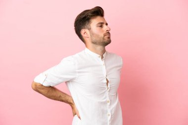 Beyaz tenli yakışıklı, pembe arka planda izole edilmiş, gayret gösterdiği için sırt ağrısı çeken genç bir adam.