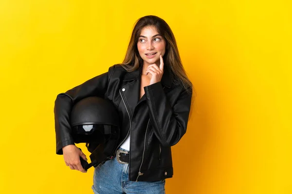 黄色の背景に隔離されたオートバイのヘルメットを持っている女性は アイデアを考えながら検索 — ストック写真