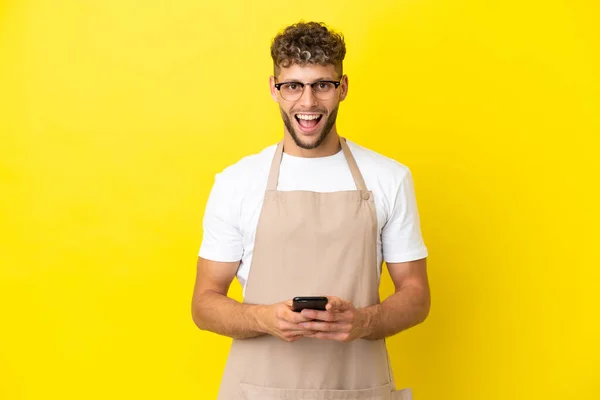 Restaurante Garçom Loiro Homem Isolado Fundo Amarelo Surpreendido Enviando Uma — Fotografia de Stock