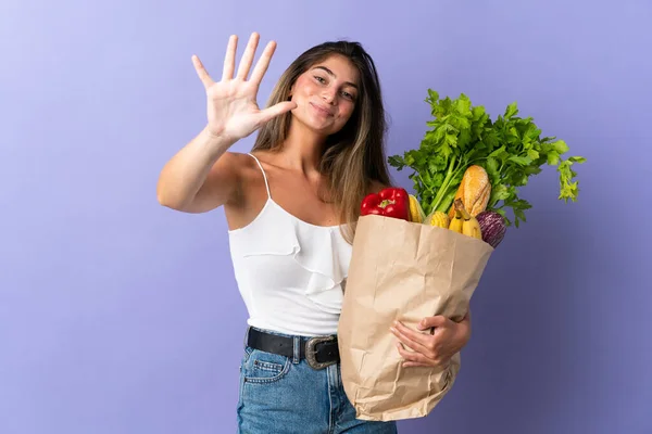 Young woman holding a grocery shopping bag counting five with fingers