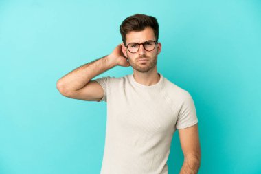 Kafkasyalı yakışıklı genç adam mavi arka planda izole edilmiş şüpheleri var.