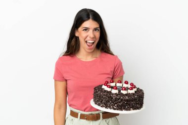 Beyaz arka planda yüzü sürpriz bir ifadeyle izole edilmiş doğum günü pastası tutan beyaz bir kadın.