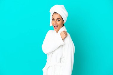 İzole edilmiş mavi arka planda bornozlu genç bir kadın zaferi kutluyor.