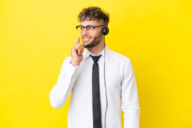 Sarı arka planda izole edilmiş bir kulaklıkla çalışan pazarlamacı sarışın bir adam yukarı bakarken bir fikir düşünüyor.